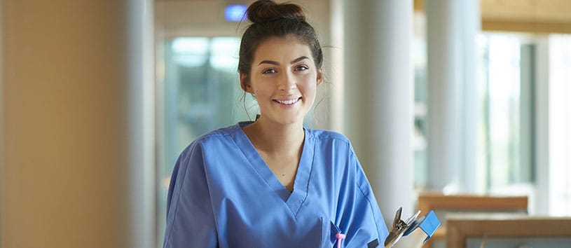 A young nursing assistant holds a clipboard and smiles. 